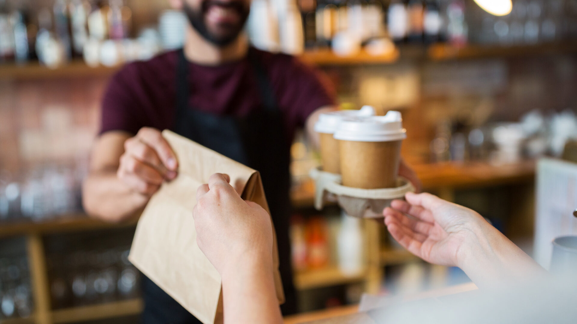 A person receiving coffees and a bag of food at a cafe