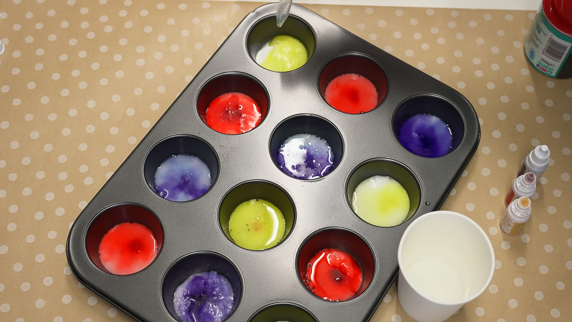a muffin tray with different coloured liquids