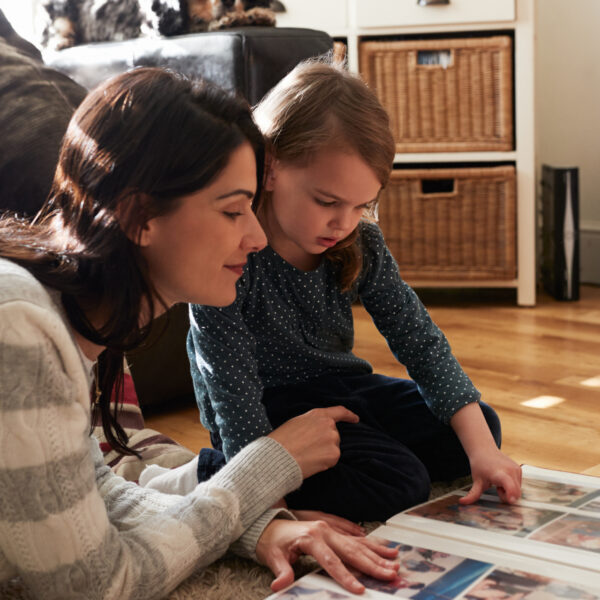 An adult lies on the floor beside a child as they both look at photos together in an album