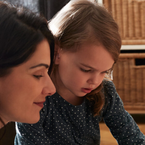 An adult lies on the floor beside a child as they both look at photos together in an album