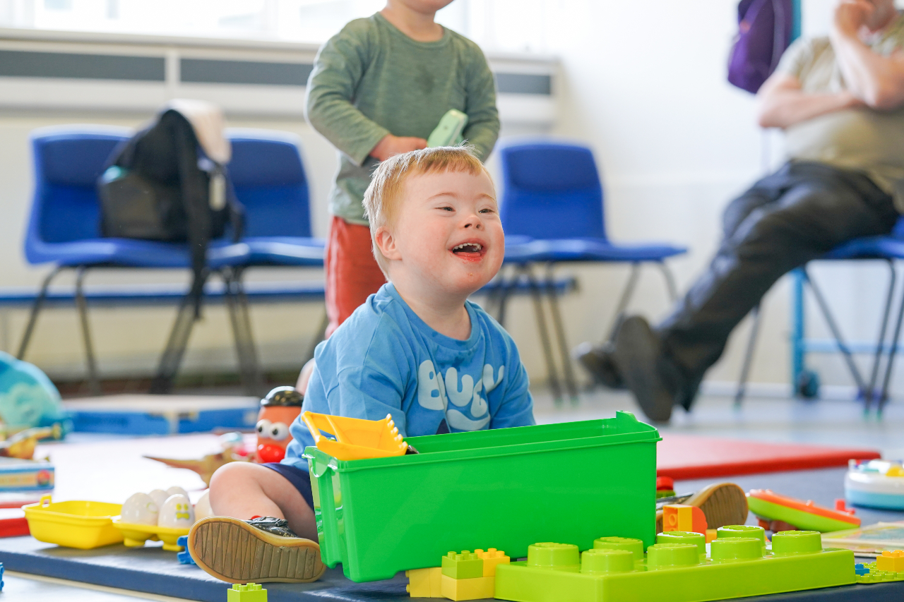 A child smiling whilst playing duplo on the floor