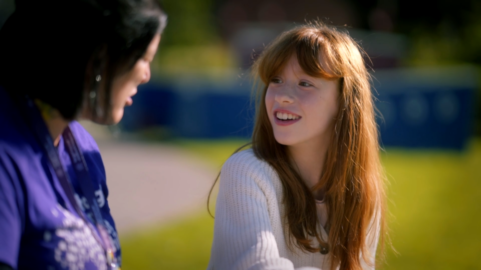 A girl smiling whilst talking to an adult in a park