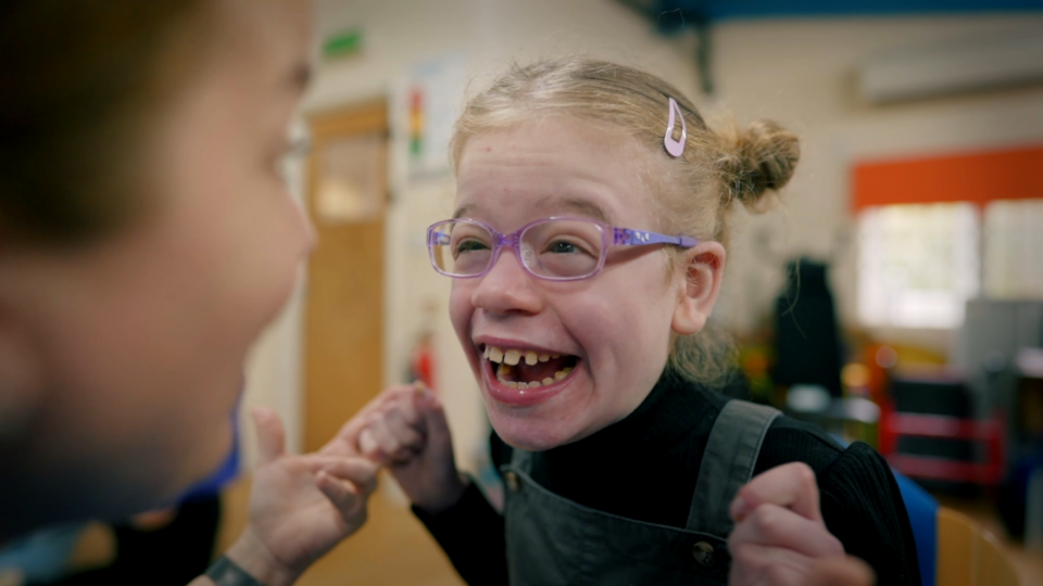 A girl wearing pink glasses and smiling whilst playing a game with an adult